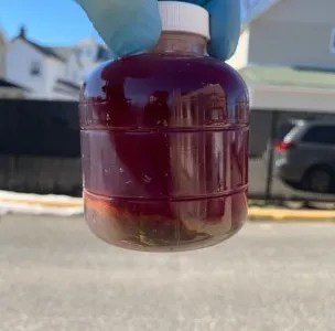 Gloved hand holding a fuel sample bottle of dark fuel with settled sediment