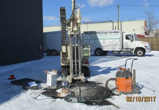 Track-mounted Geoprobe drill rig on a snowy lot beside a G.C. Environmental hazmat truck