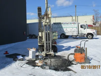 Track-mounted soil boring rig drilling a snow-covered lot beside a GCE box truck