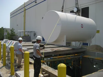 Crew guiding a new white aboveground tank lowered onto its pad