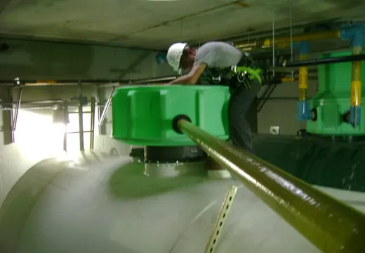 Technician in a safety harness working atop a green tank sump in an underground vault