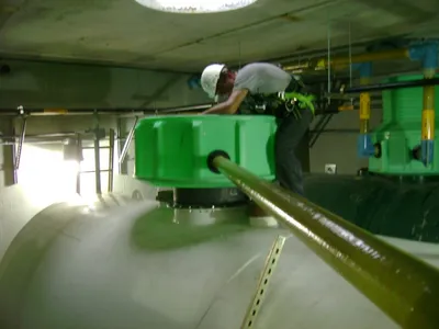 Worker servicing a green containment sump atop a horizontal tank indoors