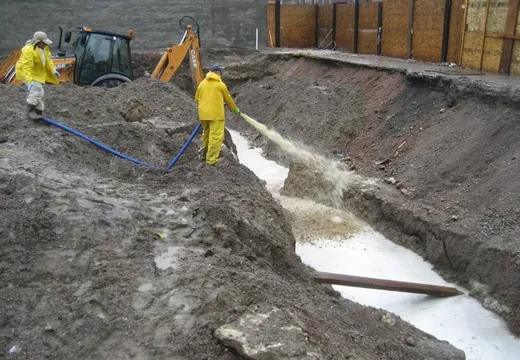 Workers in rain gear discharging pumped groundwater into an absorbent-lined excavation trench