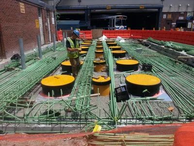 Worker among rows of tank manways and green piping in an open pit