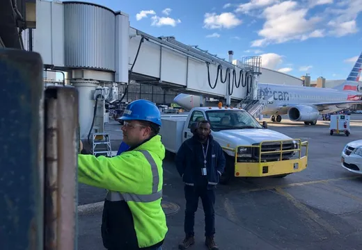 Two workers inspecting fueling equipment beside an airliner at a gate
