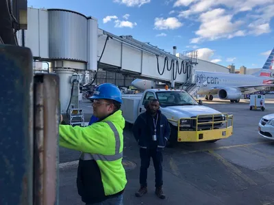 Two workers inspecting fueling equipment beside an airliner at a gate