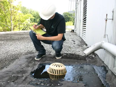 Inspector crouching to document a ponding rooftop drain during a site assessment