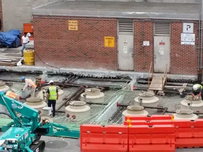 Crew installing concrete manway collars over new tanks at an urban site