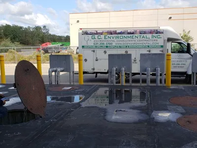 Inspector crouched at an open tank manway beside a G.C. Environmental truck