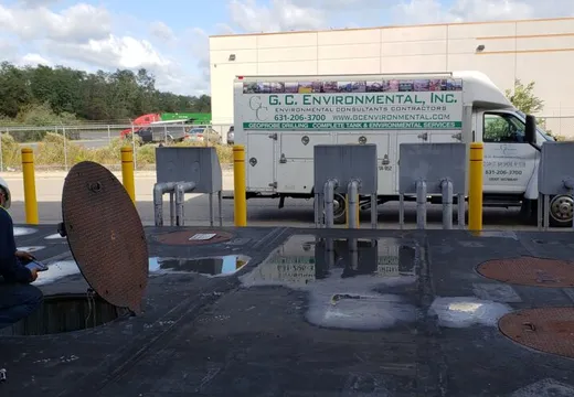 Inspector crouched at an open tank manway beside a G.C. Environmental truck
