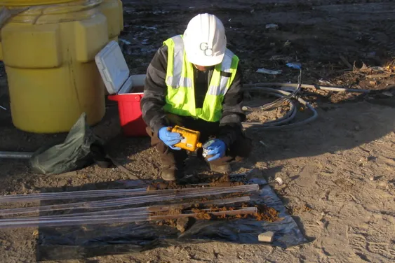 GCE technician examining soil-core samples laid out on plastic at a drilling site