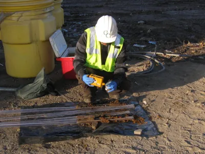 GCE technician screening soil cores laid out on plastic beside a sample drum and cooler