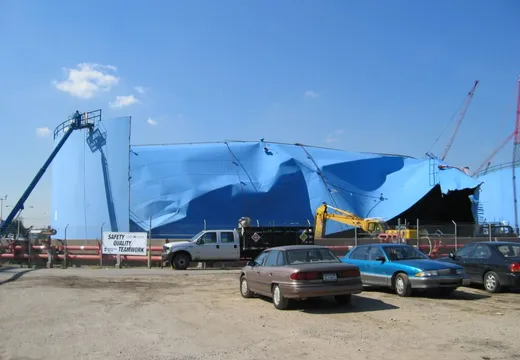 Large blue field-erected tank under containment wrap with an aerial lift on site