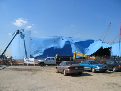 Boom lift and crew dismantling a large blue field-erected storage tank