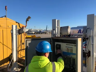 Worker operating a Veeder-Root tank monitor console on an airport ramp