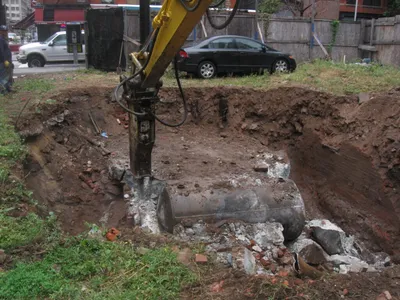 Excavator hydraulic breaker uncovering a buried tank on a city redevelopment site