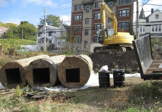 John Deere excavator beside large concrete drywell rings removed at an urban site