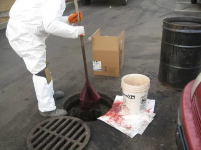 Technician in Tyvek suit pumping fluid from an open storm drain into a drum